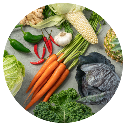 A table of BIBIBOP bowl ingredients including a bunch of carrots, kale, corn, peppers, ginger, and garlic