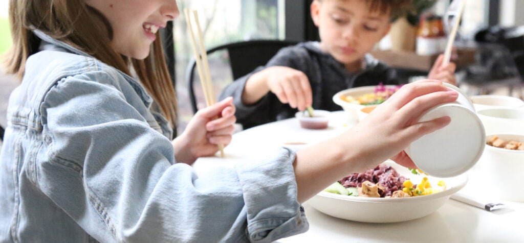 A Charley's Foundation picture showing two children eating BIBIBOP bowls with chopsticks.