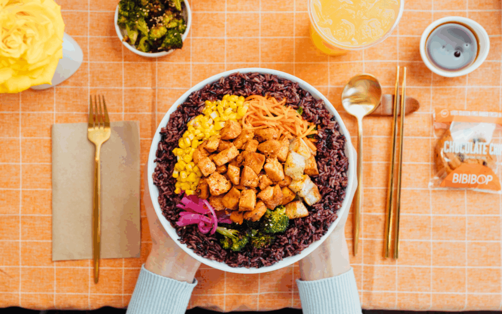 Holding a BIBIBOP bowl with side dishes and a drink