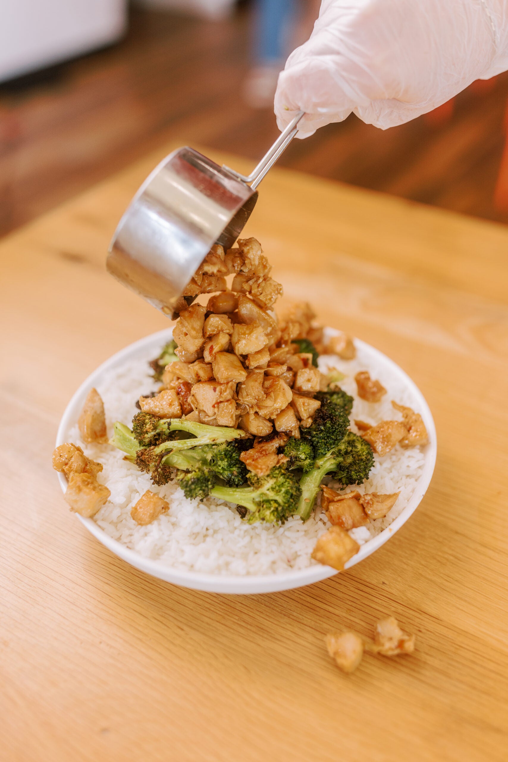 Cup of protein pouring onto bowl of rice and broccoli
