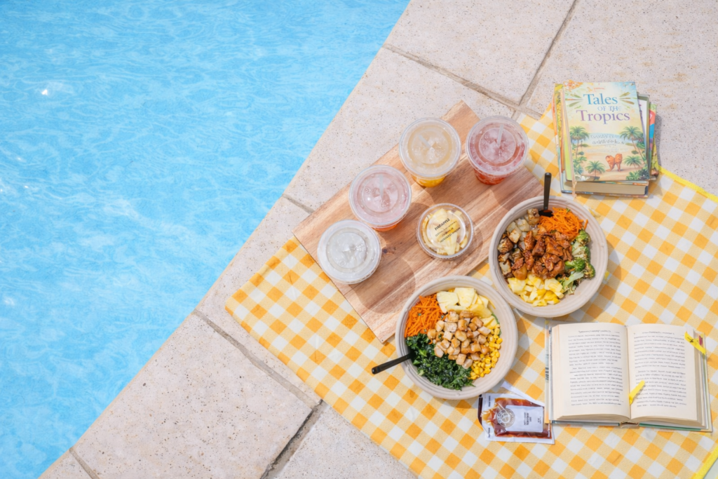 Two BIBIBOP bowls with drinks and books sitting poolside
