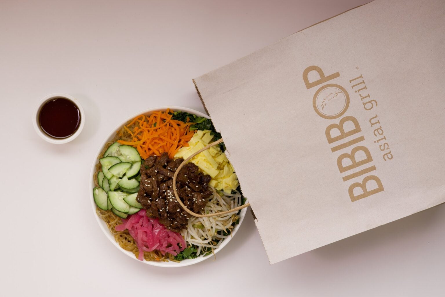 A BIBIBOP bowl with the toppings arranged in sections over noodles, with Cucumber, Carrots, Kale, Bean Sprouts and Pickled Red Onion